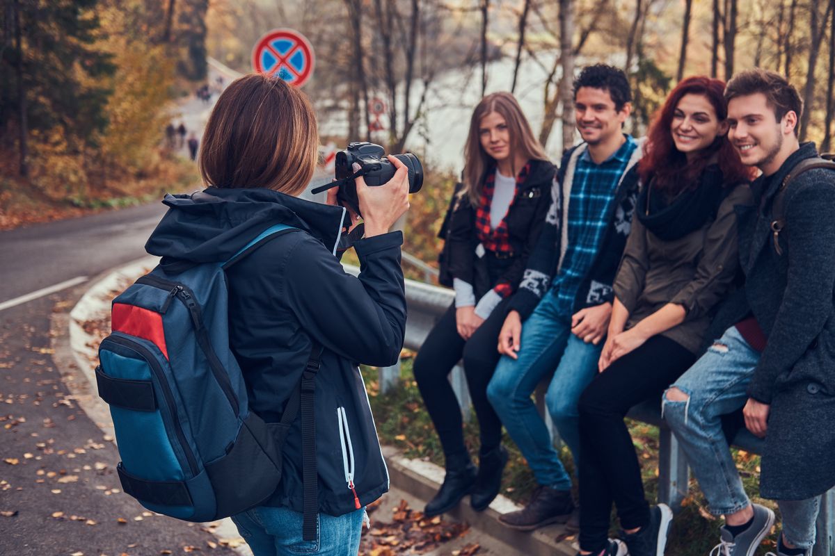 Group of young friends with backpacks sitting next to a road in forest